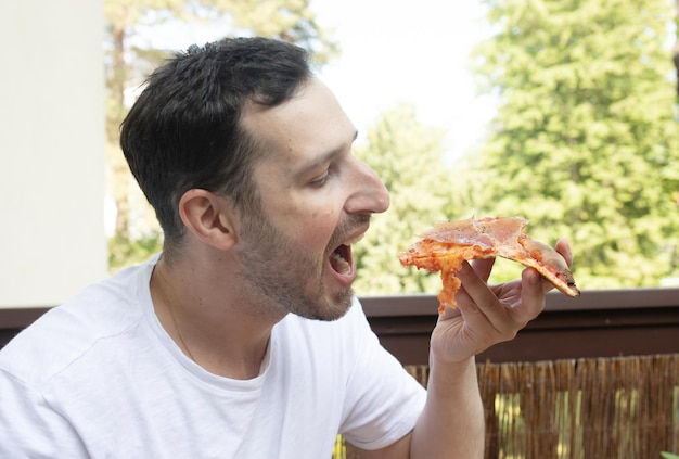 Um homem comendo uma fatia de pizza em um deck