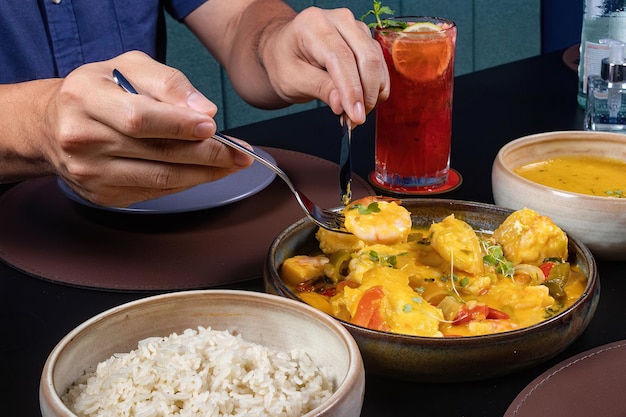 Um homem comendo uma refeição com um garfo e uma tigela de arroz.