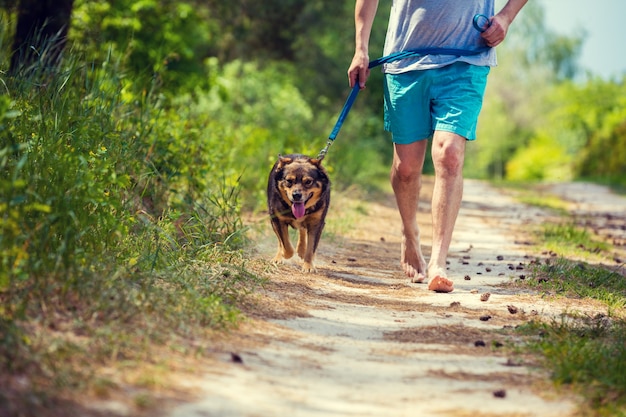 Um homem corre descalço com um cachorro em uma estrada de terra no verão