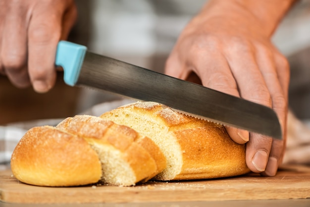 Um homem corta o pão com uma faca serrilhada.