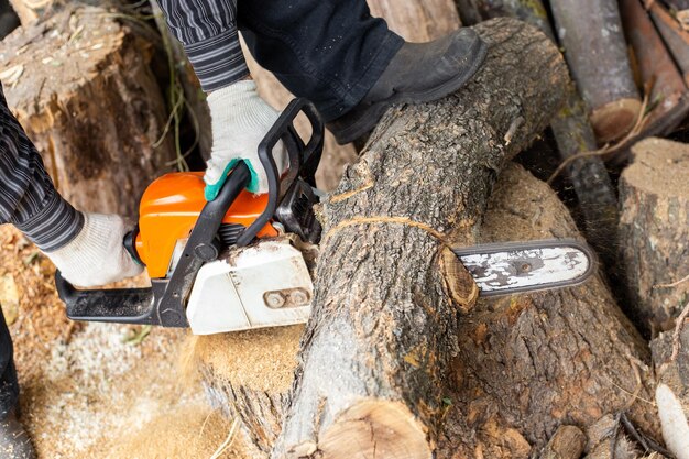 Um homem corta um tronco com uma serra elétrica preparando lenha para o inverno para aquecer a casa