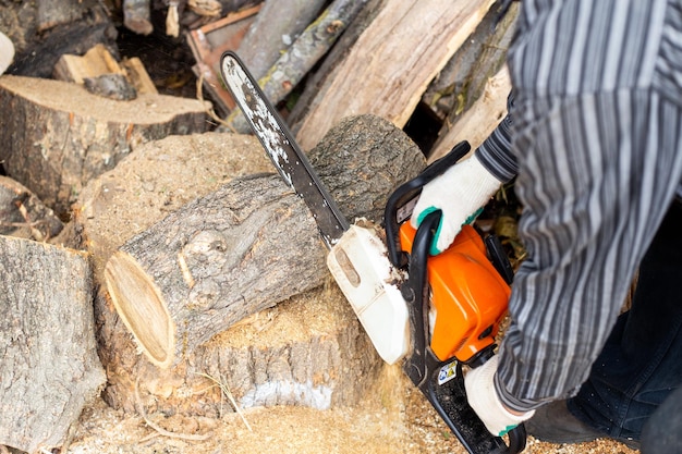 Um homem corta um tronco com uma serra elétrica preparando lenha para o inverno para aquecer a casa