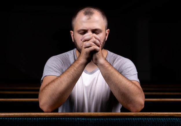 Um homem cristão de camisa branca está sentado e orando com coração humilde na igreja