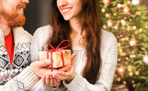 Um homem dá um presente de natal para uma mulher no fundo de uma árvore de natal