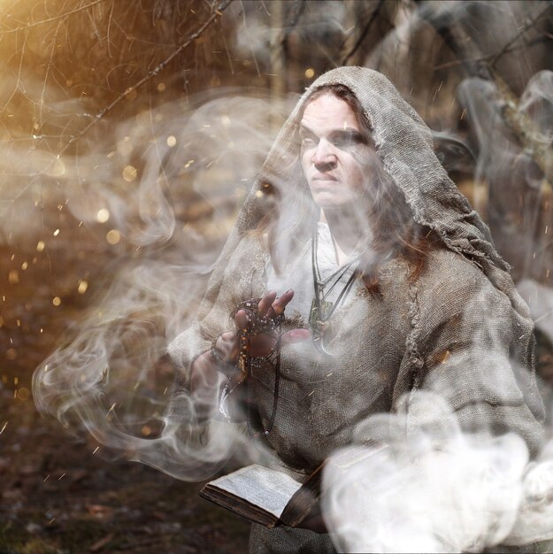 Foto um homem de batina faz um ritual em uma floresta escura com uma bola de cristal e um livro