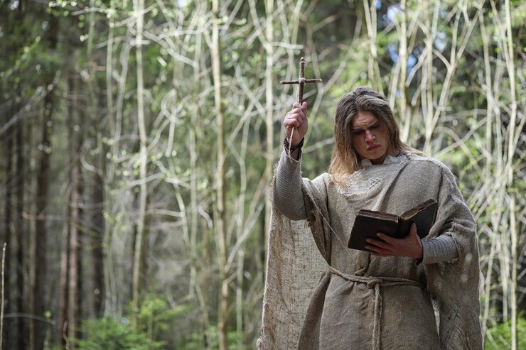 Foto um homem de batina faz um ritual em uma floresta escura com uma bola de cristal e um livro