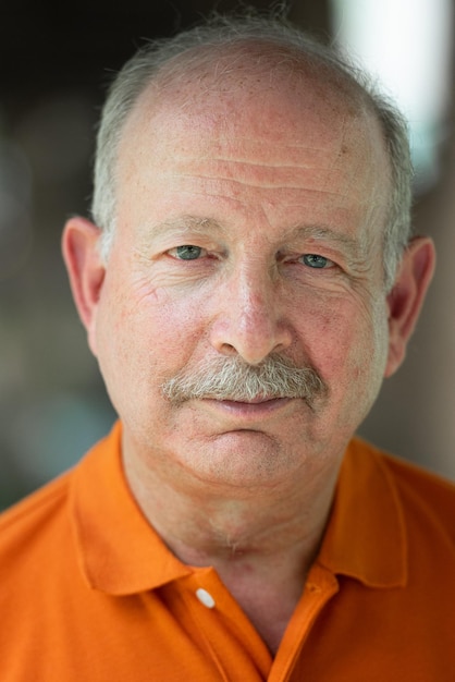 Um homem de bigode vestindo uma camisa laranja com um botão azul.