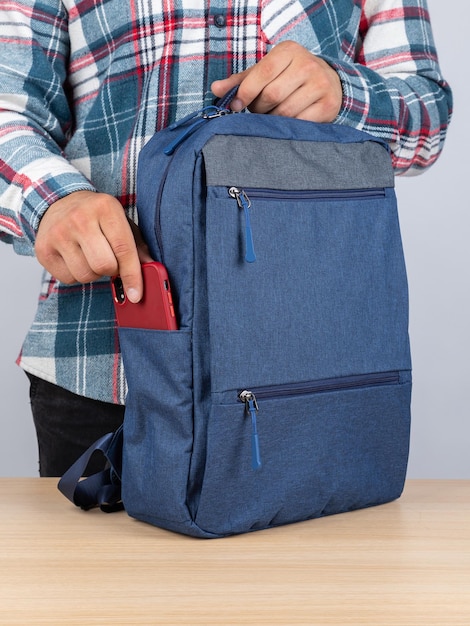 Um homem de camisa a quadros tira um telefone de uma mochila elegante para o trabalho