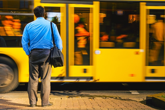 Um homem de camisa azul na agitação da cidade contra um ônibus que passava. homem perto da estrada vista de trás. homem cansado retorna do trabalho de escritório. conceito de rotina de trabalho.