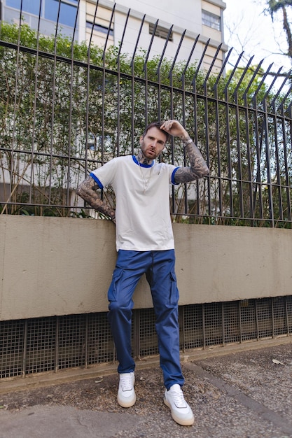 Foto um homem de camisa branca fica contra uma cerca e se inclina contra uma parede.