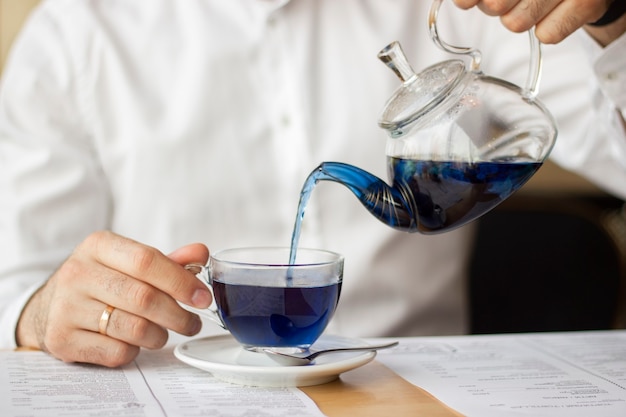 Foto um homem de camisa branca serve chá chinês azul de um bule transparente em uma caneca