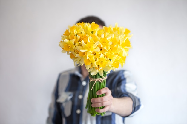 Um homem de camisa cobre o rosto com um buquê de flores. O conceito de saudações e dia da mulher.