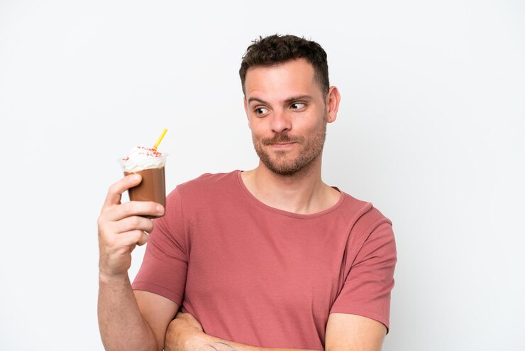 Foto um homem de camisa rosa está segurando um milk-shake de chocolate com um canudo olhando para ele