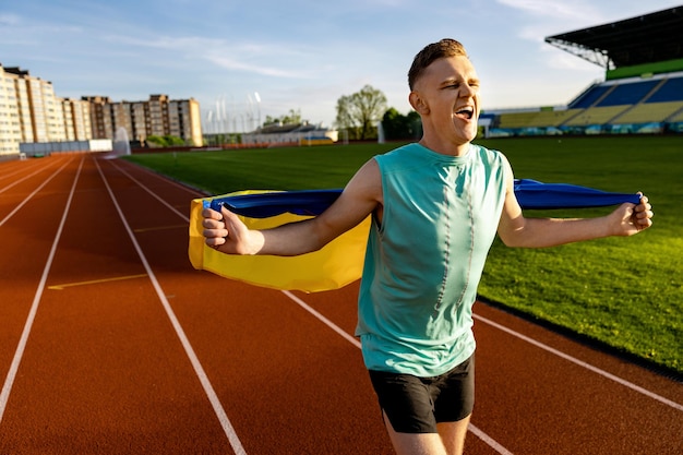Um homem de camisa verde está correndo em uma pista com uma bandeira amarela que diz 'eu sou um campeão'