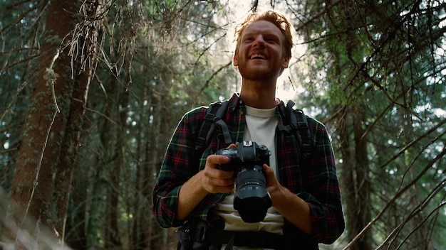 Foto um homem de camisa xadrez segura uma câmera em uma floresta.