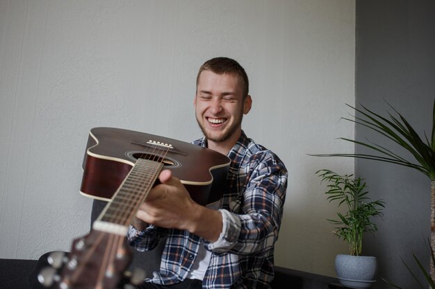 Um homem de camisa xadrez segura uma guitarra e ri