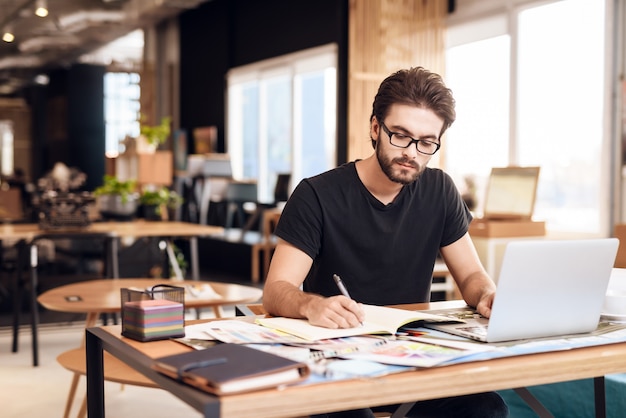 Foto um homem de camiseta preta se senta à mesa e trabalha.