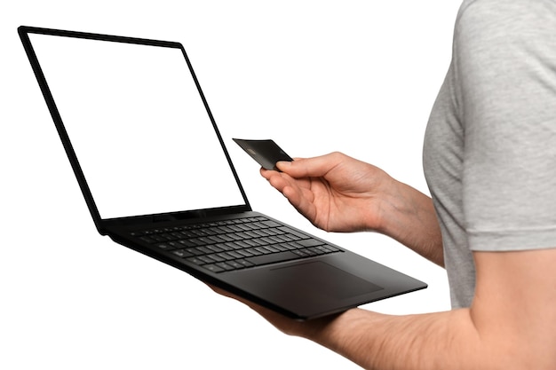 Um homem de camiseta segura um laptop, um ultrabook e um cartão bancário com a segunda mão faz uma compra online