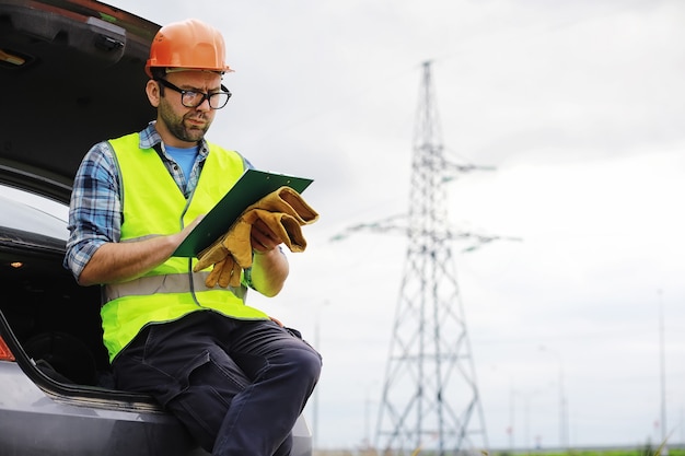 Um homem de capacete e uniforme, eletricista de campo. Engenheiro eletricista profissional inspeciona linhas de energia durante o trabalho.