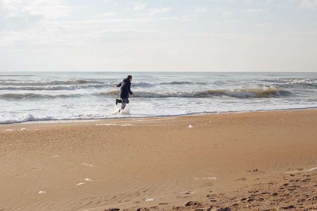 Um homem de casaco corre pela água do mar Viagens e turismo Felicidade e liberdade