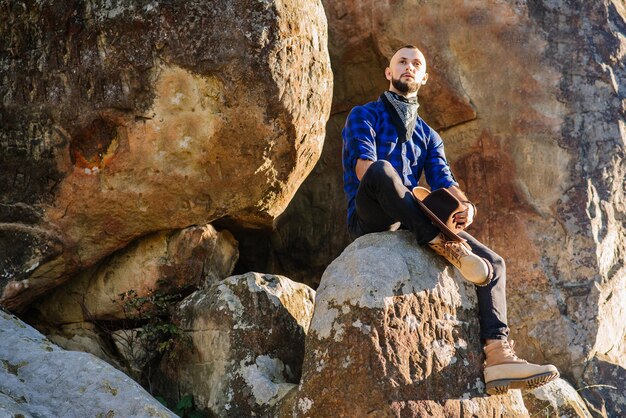 Um homem de chapéu sentado no alto das rochas no fundo do céu azul