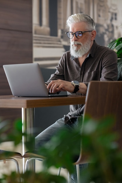 Um homem de cinquenta anos de idade, incrivelmente lindo e estiloso de cabelos grisalhos, trabalhando com um laptop