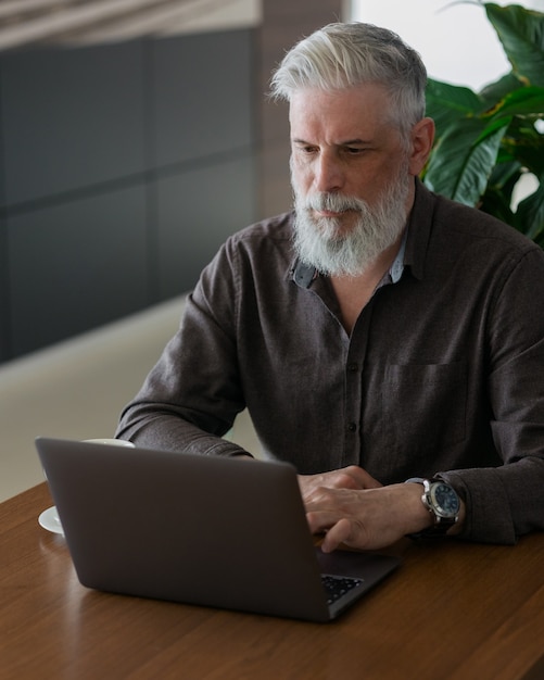 Um homem de cinquenta anos de idade, incrivelmente lindo e estiloso de cabelos grisalhos, trabalhando com um laptop