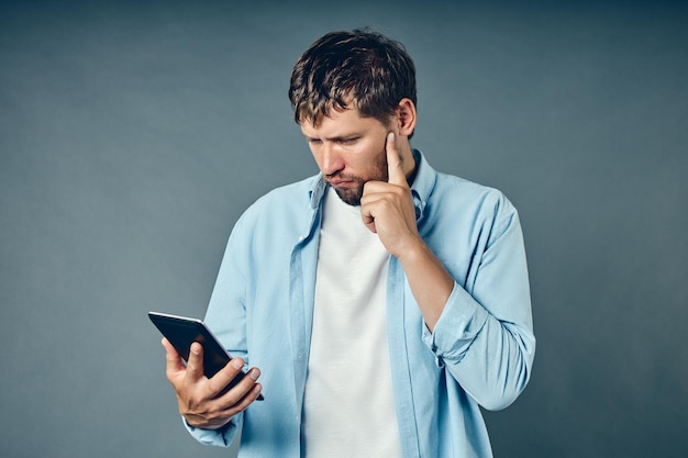 Um homem de fundo cinza segura um tablet na mão e olha pensativo para ele Dúvidas sobre a escolha do serviço