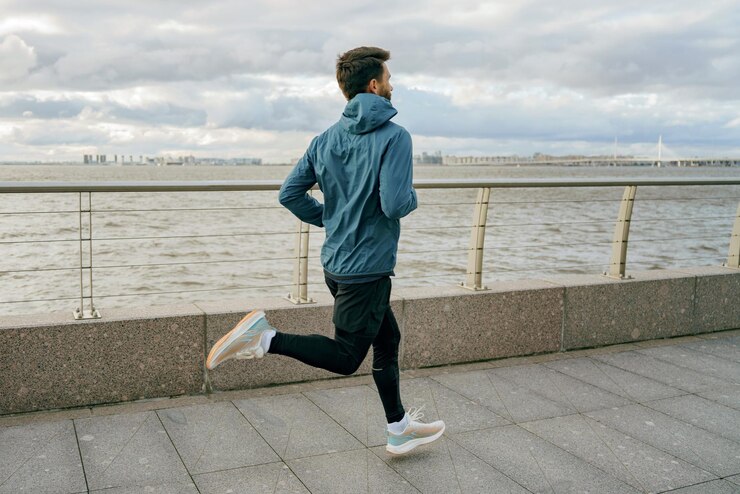 Foto um homem de jaqueta azul corre ao longo de um calçadão à beira do rio com um céu nublado dramático por cima