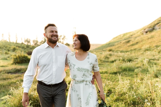 Um homem de meia-idade abraça uma mulher de aparência europeia que segura nas mãos as flores do marido. retrato de um casal apaixonado ao pôr do sol