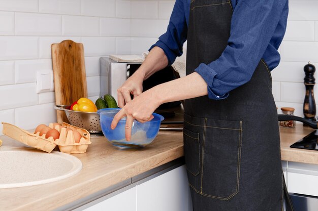 Um homem de meia idade bate um ovo com um batedor para fazer uma omelete na cozinha