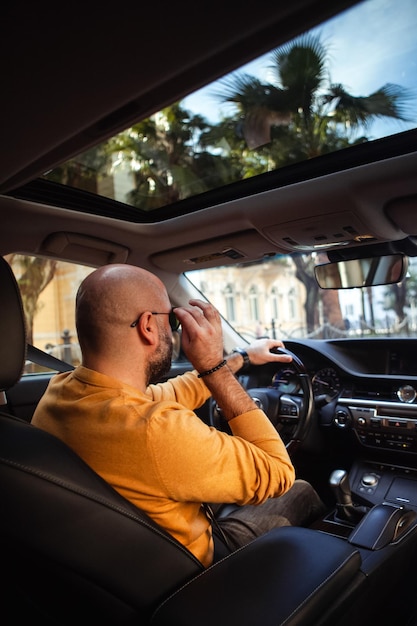 Um homem de meia-idade careca conduz um carro.
