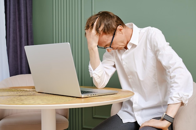 Um homem de meia-idade chateado e cansado com um portátil baixa a cabeça.