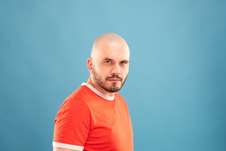 Foto um homem de meia-idade com barba em uma camiseta vermelha em uma parede azul está com os braços estendidos e se alegra com a vitória. isolado.