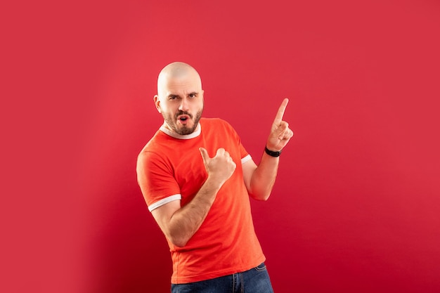 Um homem de meia-idade com barba em uma camiseta vermelha em uma parede vermelha está exultante com a vitória. Isolado.