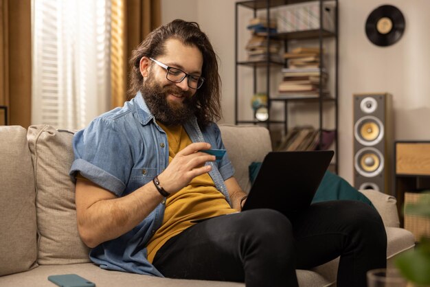 Foto um homem de meia idade com barba usa um laptop enquanto está sentado no sofá na sala de estar um estudante