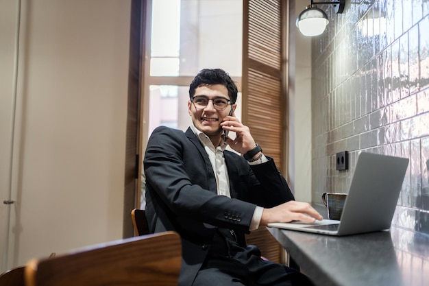 Um homem de negócios com óculos de terno usa um laptop funciona em um espaço de coworking de escritório