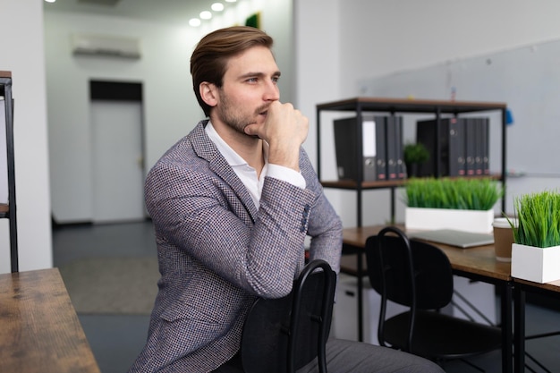 Um homem de negócios em uma jaqueta senta-se em uma cadeira no pensamento do escritório olha para frente