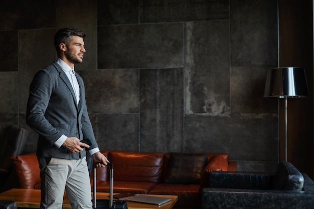 Um homem de negócios formalmente vestido carrega bagagem e um telefone celular no saguão do hotel