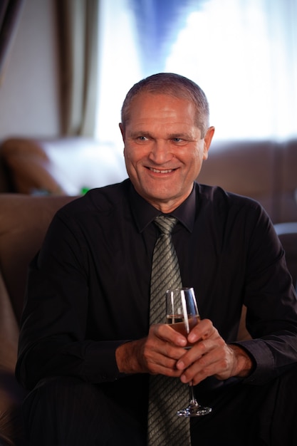 Um homem de negócios idoso com uma camisa preta sorrindo, sentado com uma taça de vinho na mão