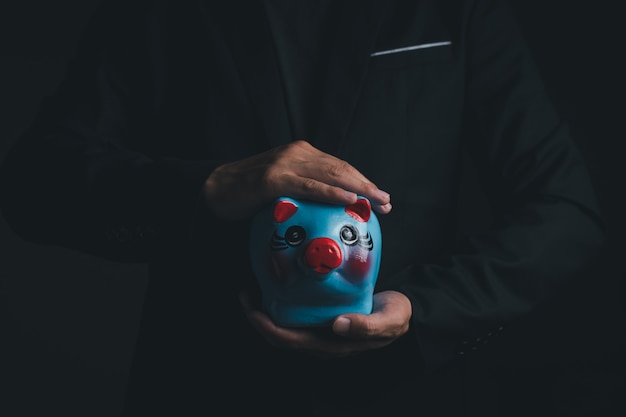 Um homem de negócios segurando o porquinho azul poupança, close-up tiro com espaço de cópia para texto individual, poupança e conceito de investimento