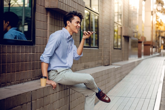 Foto um homem de negócios sorridente using voice control via smartphone.