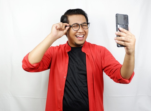um homem de óculos e camisa vermelha segura um telefone com a mão na orelha.