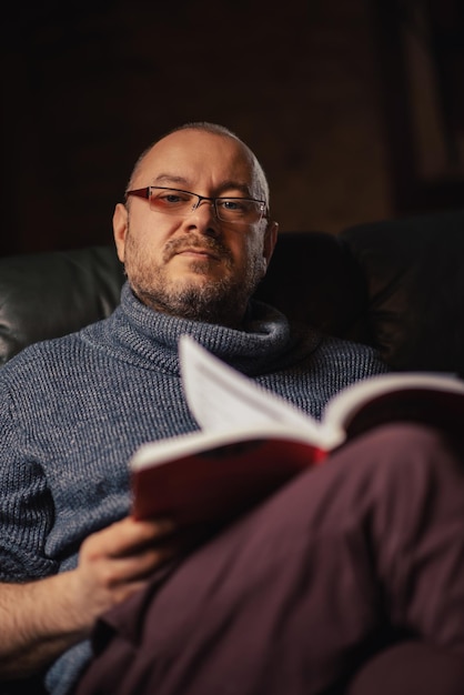 Um homem de óculos está lendo um livro Homem de meia-idade de aparência comum em roupas casuais em casa Leitura aprendendo