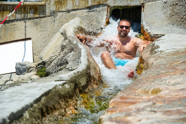 Um homem de óculos está sentado sob uma cachoeira de água curativa com fontes termais em Pamukkale. Turquia.