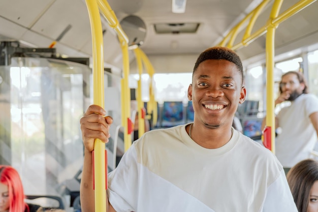 Um homem de pele escura fica no meio de um ônibus indo para casa, ele está sorrindo