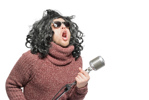 Um homem de peruca, suéter e óculos escuros cantando em um microfone Isolado