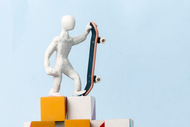 Um homem de plasticina branca está de pé em cima de cubos em um fundo azul e segurando um skate em uma mão. conceito de motivação, sucesso, realização do objetivo definido.