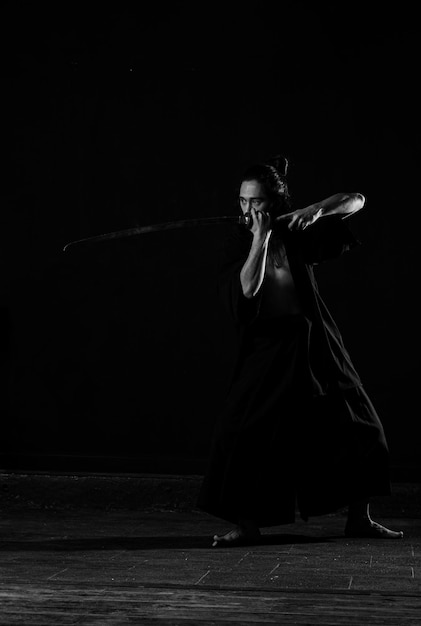 Um homem de quimono preto com uma espada na mão.