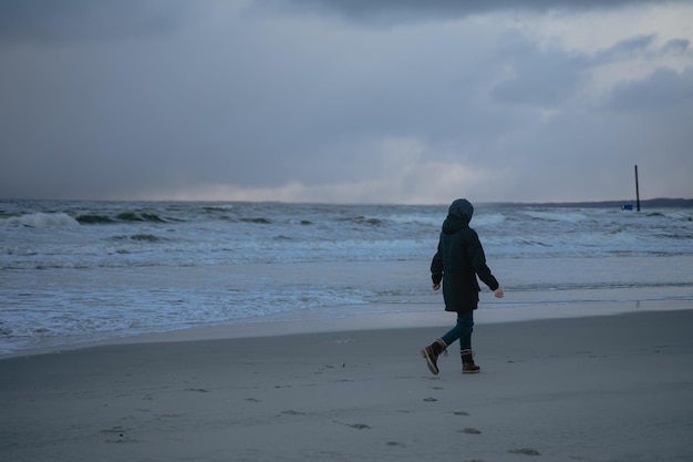 Um homem de roupas pretas caminha sozinho em uma praia vazia do mar